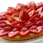 Tarte aux fraises garnie de crème et de fraises fraîches disposées sur la pâte, servie sur une nappe blanche
