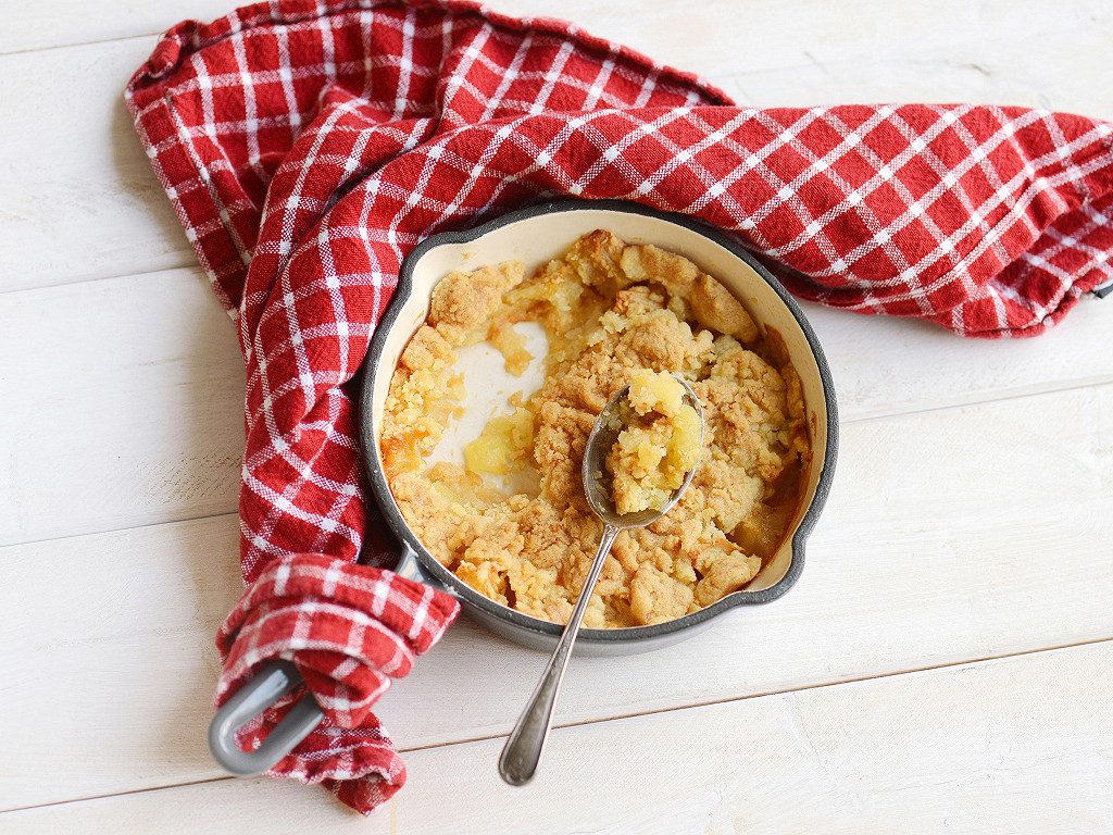 Une image d'illustration montrant un crumble aux pommes déjà entamé par une cuillère, dans un plat chaud